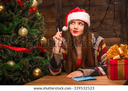 New Year and Christmas concepts. Beautiful girl thinking about New Year and Christmas congratulation for someone. Pretty lady sitting at the table.
