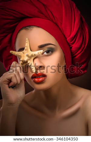 Close-up portrait of beautiful girl with red lips holding starfish. Attractive lady with tattoos looking at the camera.