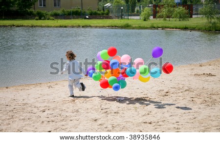 little boy runs with helium bubbles on sand to lake bank