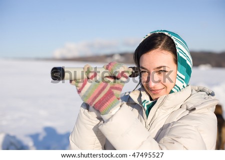 Positive girl in kerchief take a look in spyglass on snowy field