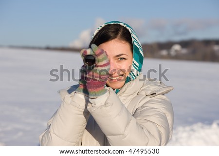 Positive girl in kerchief take a look in spyglass on snowy field