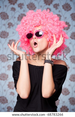 Funny girl in pink wig and glasses posing for camera across wallpapers background