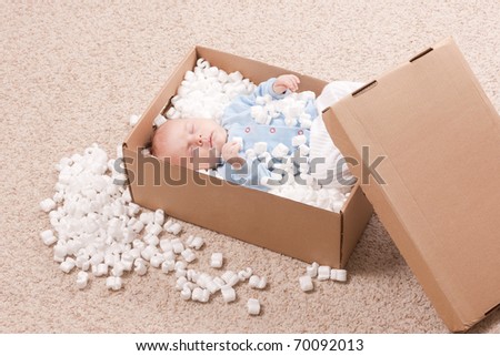 Newborn baby in open post box with filler on carpet