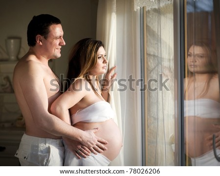 Happy family - pregnant wife and husband near window