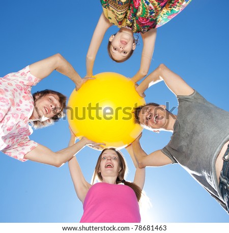 Group of young people hold big yellow ball across blue sky