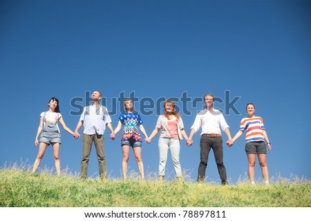 Group of people on hill hold hands together across blue sky