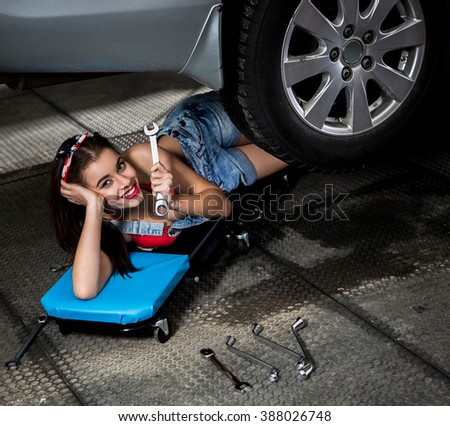 Portrait of car mechanic woman lying ubder car and holding wrench for repairing car at repair shop or service station.
