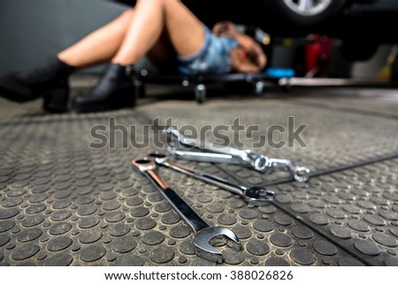 Close-up portrait of diagnostic tools for car repairing at garage while lady lying under car on background.