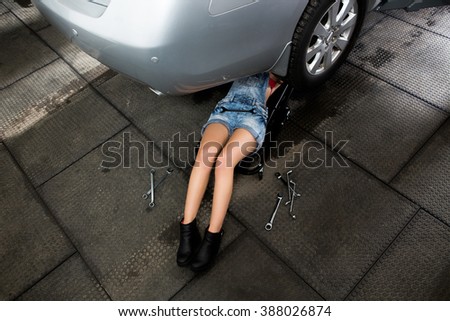 Mechanic lying and looking under car at repair garage. Young lady trying to solve the problem with car at service station.