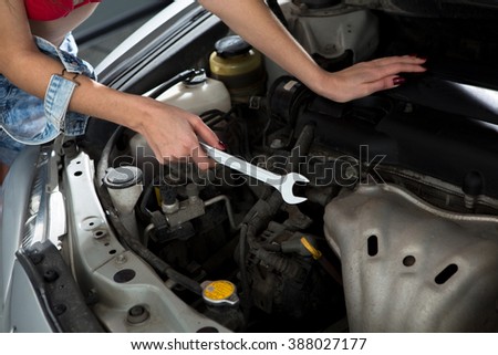 Portrait of car mechanic woman repairing electronic motor while holding wrench in front of her at repair shop.