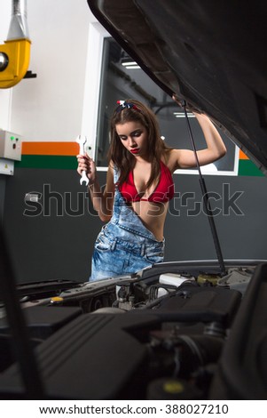 Nice young woman repairing car at servie station. Female mechanic fixing a car at garage.