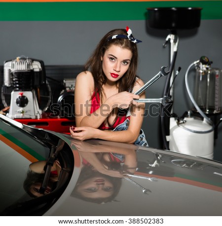 Car mechanic woman working with wrenches in repair shop while automatic lubrication system on background.