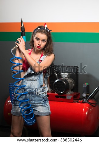 Sexy lady in jeans posing with automotive air-conditioning compressor and screw gun in repair shop or service station.