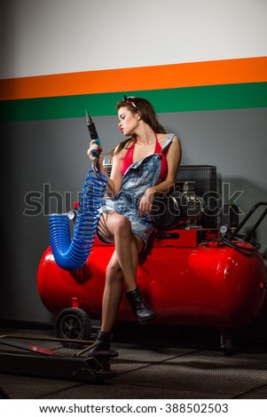 Model lady posing for magazine at service station while holding automotive air-conditioning compressor and screw gun in repair shop.