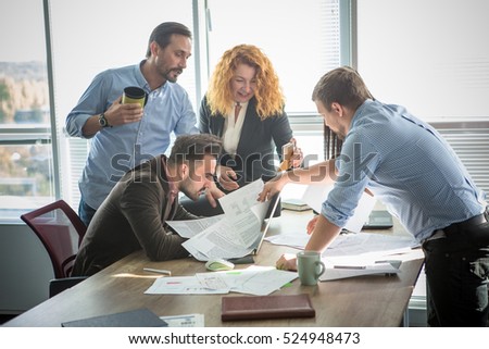 Business people looking through documents all together and happy smiling while working in team in board room in office interior. Teamwork concept.