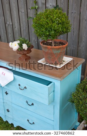 Blue, turquoise drawer with flowers, green tree, white roses, wooden background. \
One box is open.