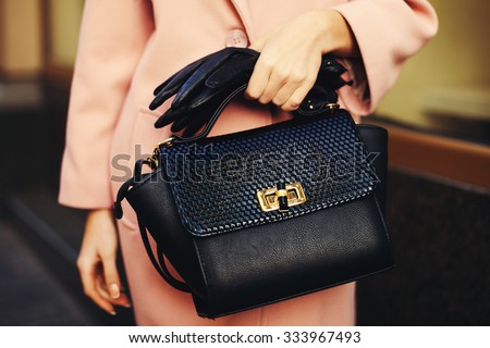 Elegant outfit. Closeup of black leather bag handbag in hand of stylish woman. Fashionable girl on the street. Female fashion. Toned
