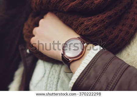 Elegant outfit. Closeup of brown wrist watch on the hand of stylish woman. Fashionable girl on the street. Female fashion. Toned