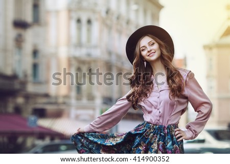 Outdoor portrait of young beautiful fashionable happy lady posing on a street of the old city. Model wearing stylish clothes. Girl looking at camera. Female fashion. City lifestyle. Copy space. Toned
