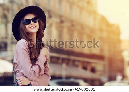Outdoor portrait of a young beautiful fashionable happy lady posing on a street of the old city. Model wearing stylish clothes. Girl looking up. Female fashion. City lifestyle. Copy space for text