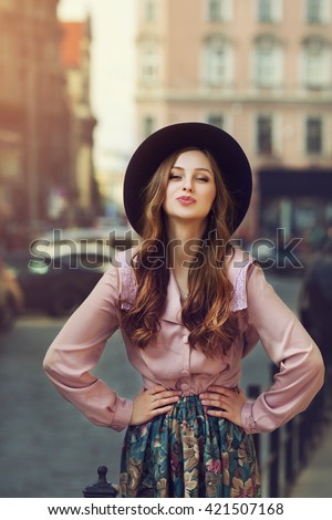 Outdoor portrait of young beautiful fashionable playful lady posing on old street. street. Model wearing stylish hat & clothes. Sunny day. Female fashion. City lifestyle. Toned style instagram filters