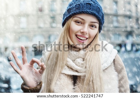 Everything is OK! Outdoor close up portrait of young beautiful happy smiling girl showing okay gesture. Model looking at camera, wearing stylish winter clothes.  Christmas, new year, concept. Snowfall