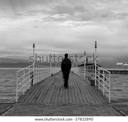 Blurred silhouette of a man on a wooden quay on a lake, black and white