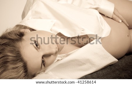 Beautiful young blond woman, seven months pregnant, in a white shirt lying down