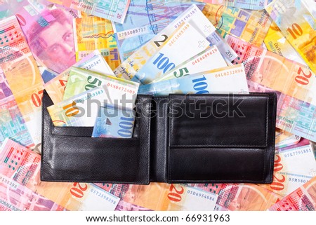 A black Wallet with Swiss Francs, is lying on a Table full of Swiss Francs