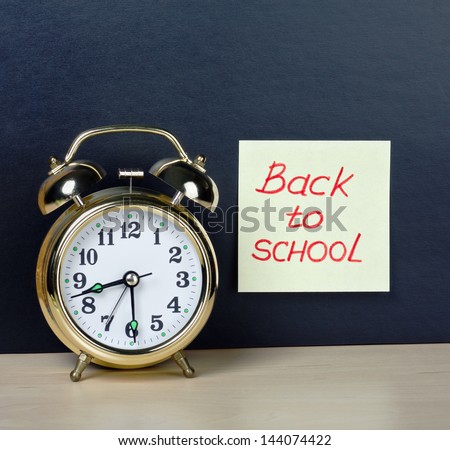 alarm clock and sticker with text back to school on the school board background