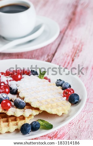 Waffles with fresh berries on the table. Focus on the blueberries and waffles in the foreground. small depth of field