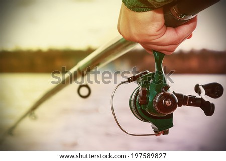 hand holding a fishing rod with reel. Focus on Fishing Reels. Toned image