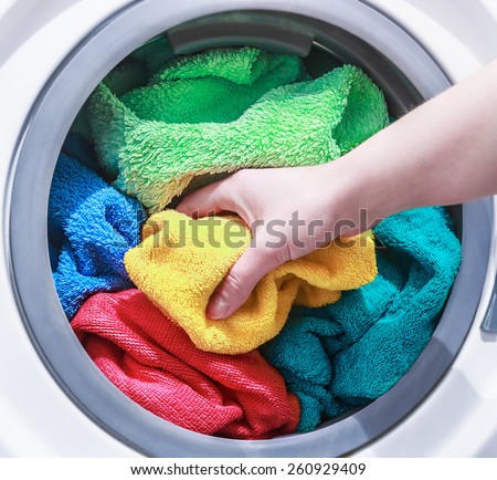 hand and puts the laundry into the washing machine. focus on a colored towel