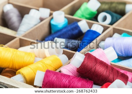 Multicolor sewing threads on wooden background. focus on the red thread