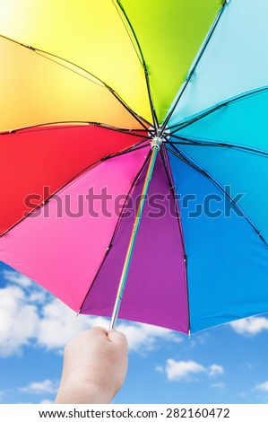 Rainbow umbrella in woman hands against cloudy sky. Focus on the latch closing umbrella