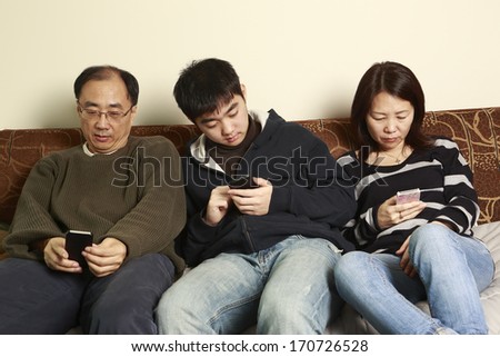 Family of three, each with a smart phone, text messaging at home,