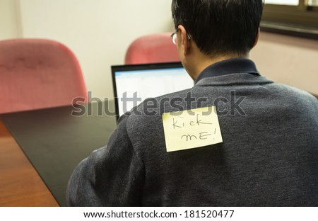 Office man with a yellow sticky note on his back, saying kick me