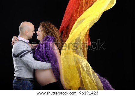 happy young family expecting a baby and posing on black background