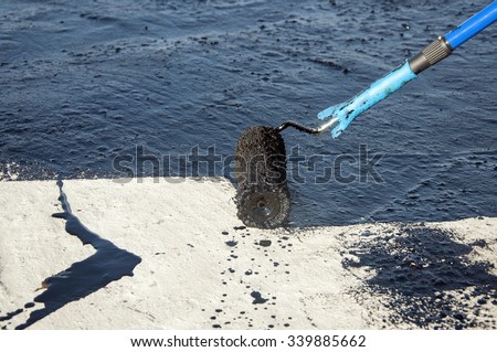 Roofer worker painting black coal tar or bitumen at concrete surface by the roller brush, Â  waterproofing