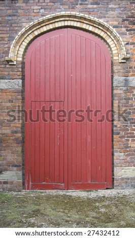 Small access door set into a large red wooden door set into a brick wall