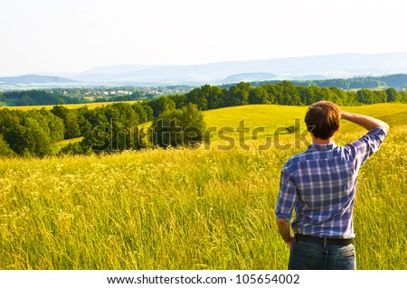 man looking far away standing on green filed