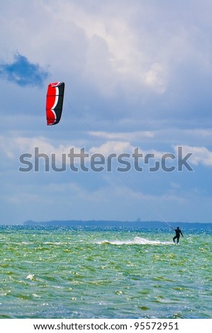 Kiter with red and black kite surfing against blue sky
