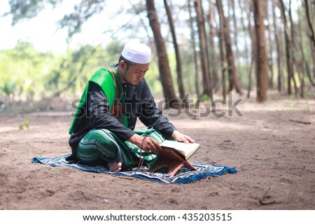 Asian man in arabic clothes reading Quran at outdoor
