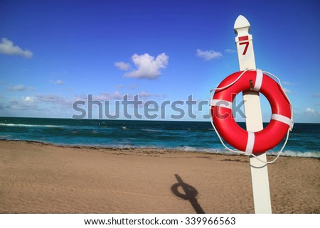 Orange lifebuoy ring, life preserver on a pole number 7. Blue sky, some clouds, sea and sun in background. Miami, Florida.