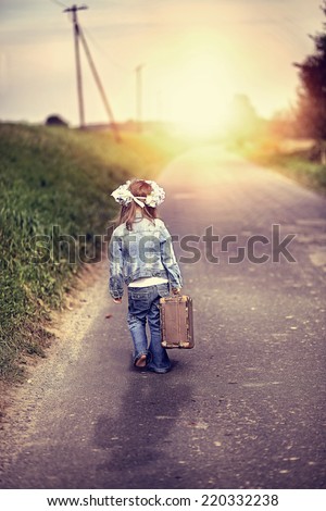 Great adventure - a girl with a suitcase walking down the street to the sunset