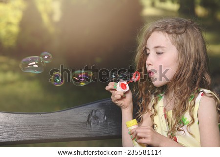 Pretty young girl lets soap bubbles in the park