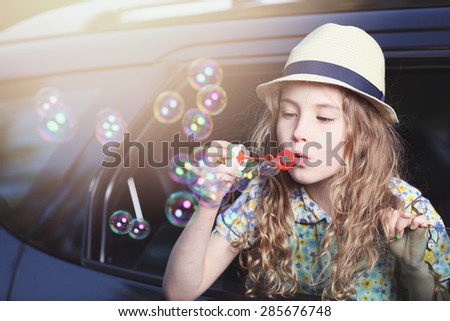 Cute little girl in a hat lets soap bubbles in car window