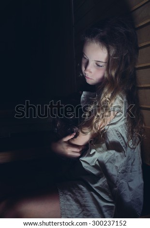 A sad little girl hugging a doll at home