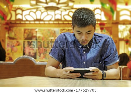 Young asian man busy with tablet computer in a restaurant.