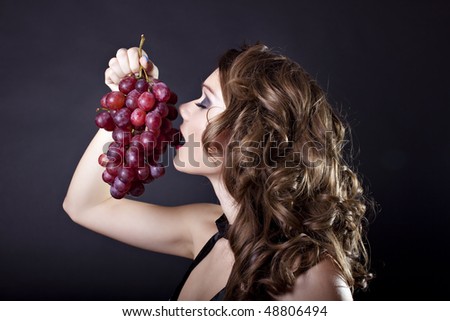 Elegant woman eating grape on black background